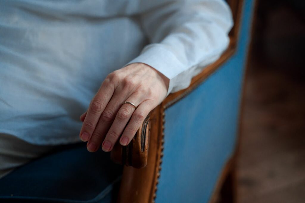 Close-up of a hand with a wedding ring resting on a blue armchair, capturing elegance and simplicity.